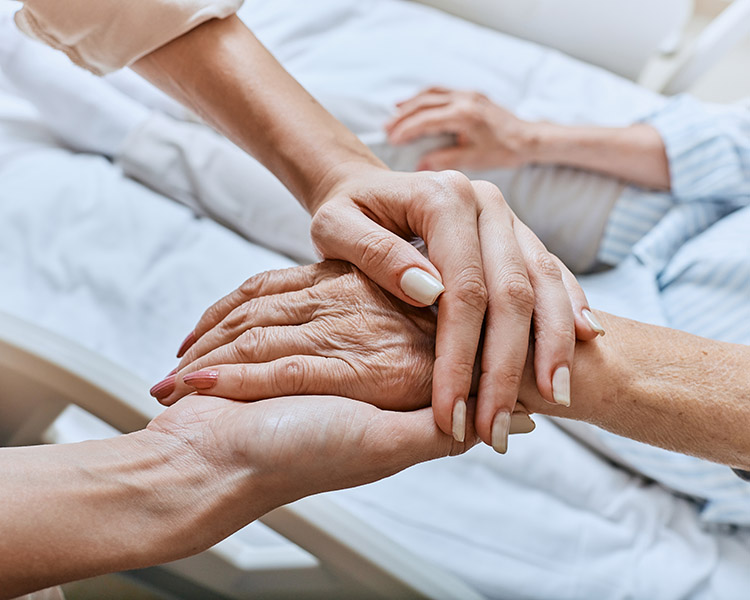 Hospiz Wetten Die Hand einer älteren Person wird fürsorglich von einer anderen gehalten